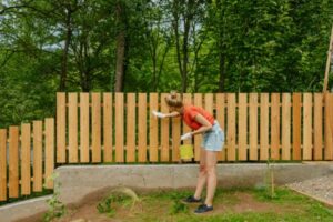 Woman Enhances the Picket Fence's Elegance with Estate Fence Paint Strokes